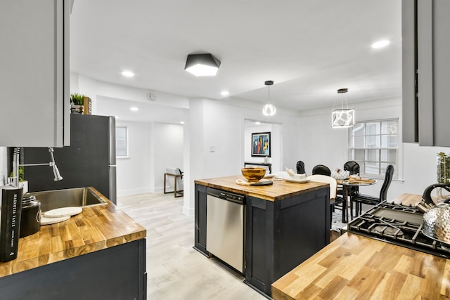 kitchen featuring dark cabinets, butcher block counters, light wood-style floors, appliances with stainless steel finishes, and pendant lighting