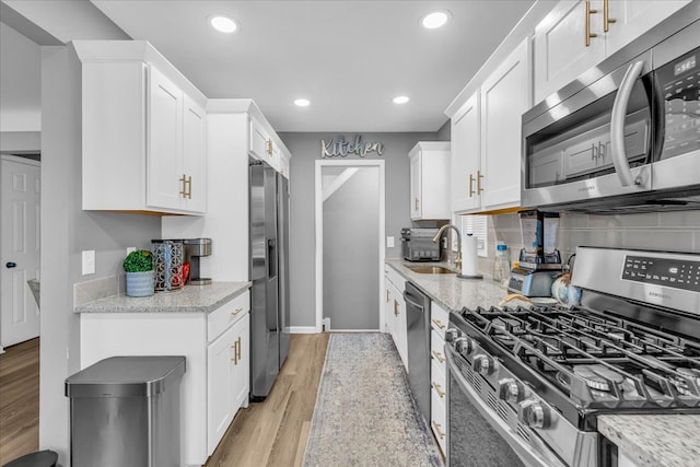 kitchen with stainless steel appliances, white cabinets, light stone counters, and light hardwood / wood-style flooring