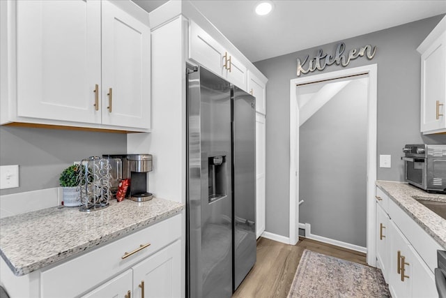 kitchen featuring light stone counters, stainless steel fridge with ice dispenser, light hardwood / wood-style floors, and white cabinets