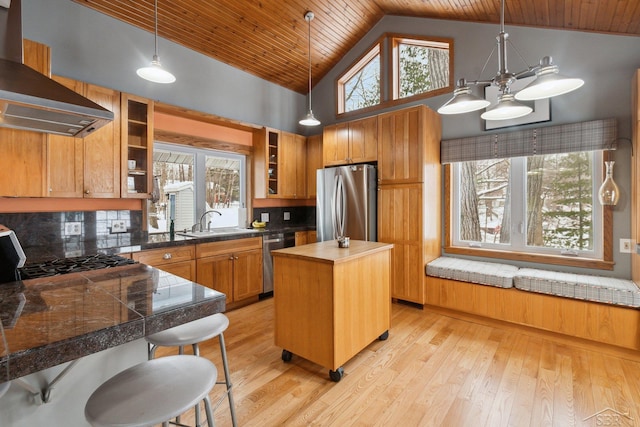 kitchen with pendant lighting, wall chimney range hood, stainless steel appliances, a center island, and a kitchen bar