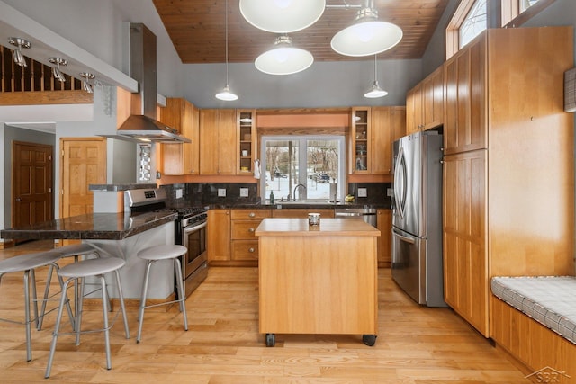 kitchen featuring pendant lighting, range hood, a kitchen bar, a center island, and stainless steel appliances