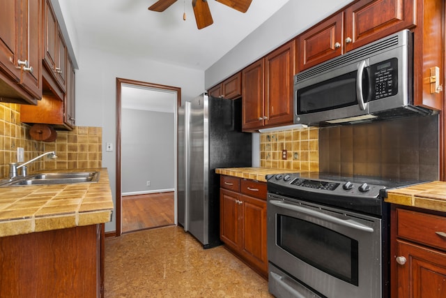 kitchen with sink, ceiling fan, stainless steel appliances, tile countertops, and decorative backsplash