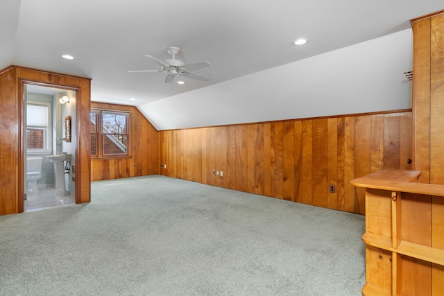 additional living space featuring light carpet, lofted ceiling, ceiling fan, and wood walls