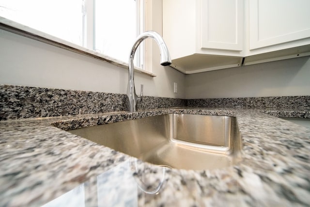 details with sink, white cabinets, and stone counters