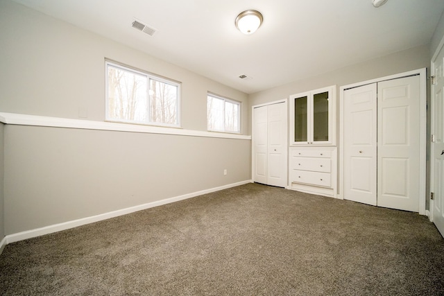 unfurnished bedroom featuring two closets and dark colored carpet