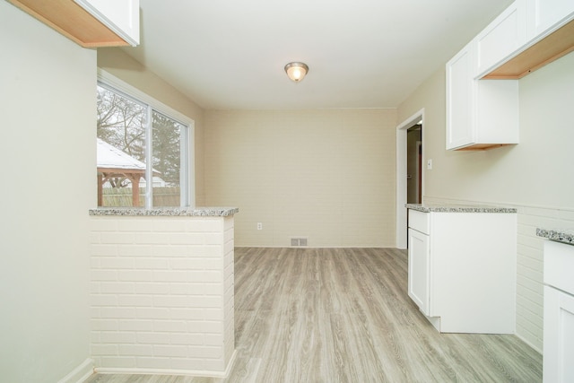 kitchen with white cabinetry, light stone counters, and light wood-type flooring