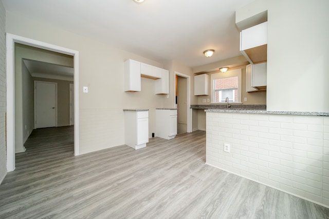 kitchen featuring sink, kitchen peninsula, light stone countertops, light hardwood / wood-style floors, and white cabinets