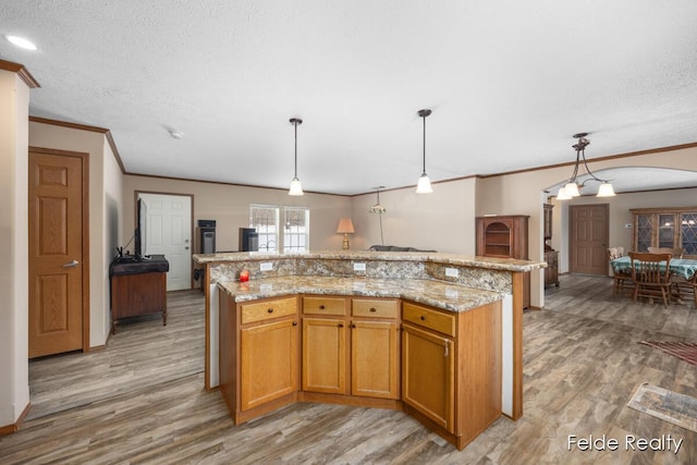 kitchen featuring a center island, ornamental molding, light hardwood / wood-style floors, a textured ceiling, and decorative light fixtures