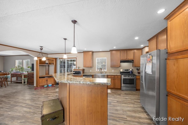 kitchen featuring pendant lighting, sink, appliances with stainless steel finishes, wood-type flooring, and light stone countertops