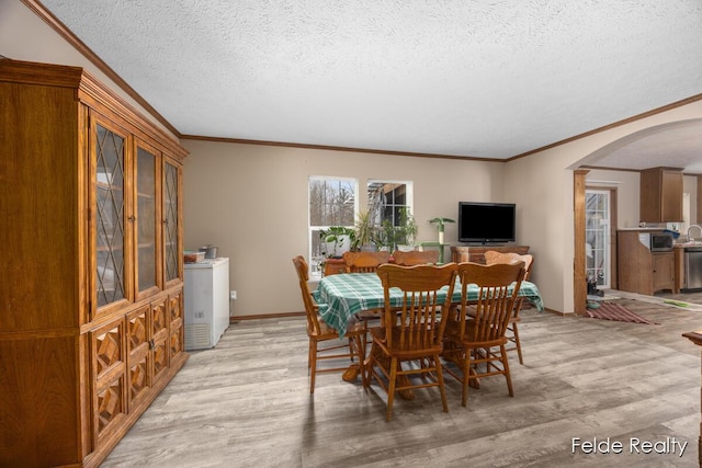 dining space with ornamental molding, a textured ceiling, and light wood-type flooring