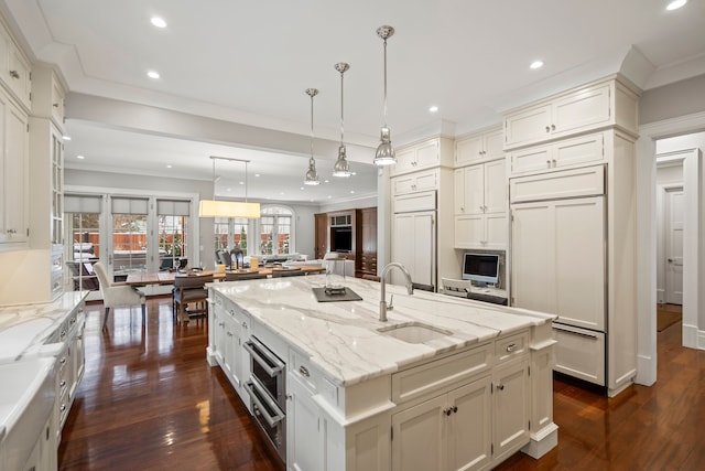 kitchen with a sink, paneled built in fridge, open floor plan, hanging light fixtures, and an island with sink