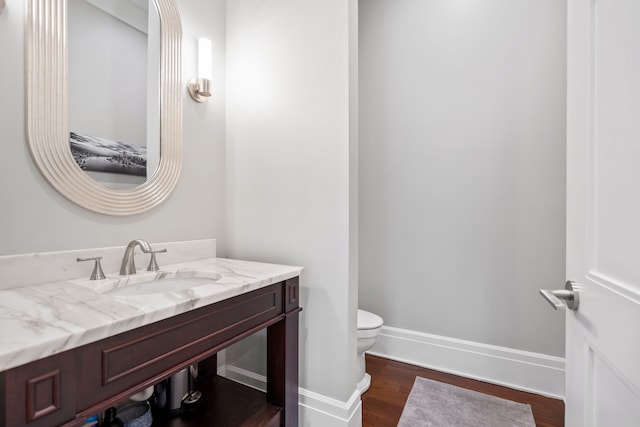 half bath featuring vanity, wood finished floors, toilet, and baseboards