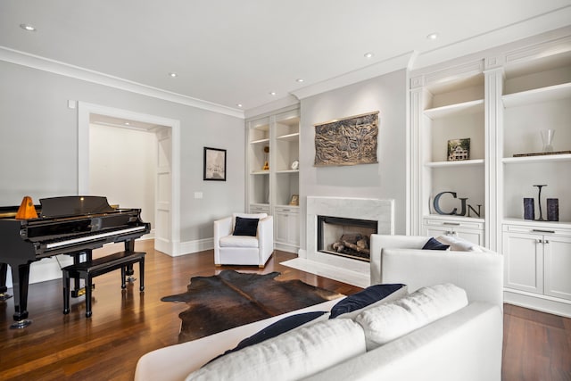 living area featuring built in shelves, dark wood-style floors, a fireplace, ornamental molding, and baseboards