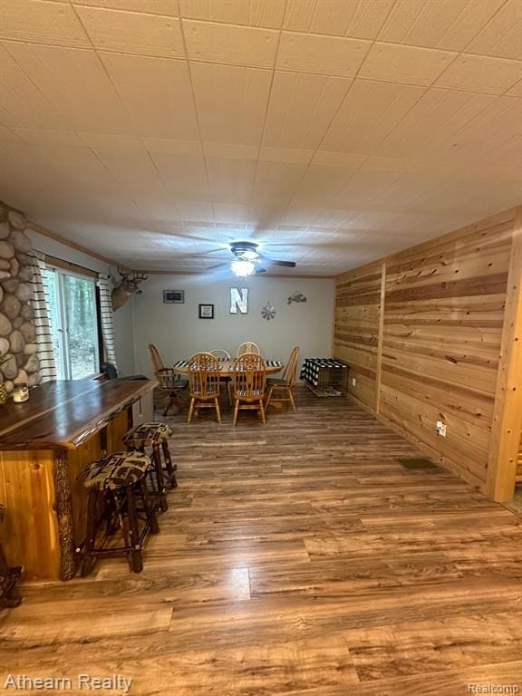 unfurnished dining area featuring hardwood / wood-style flooring, ceiling fan, indoor bar, and wood walls