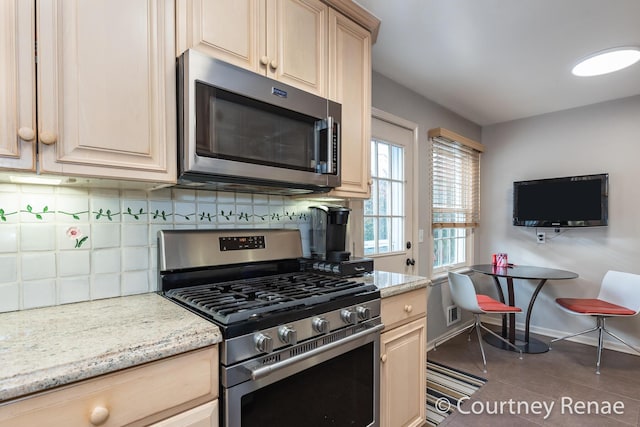 kitchen with light brown cabinetry, dark tile patterned floors, stainless steel appliances, light stone countertops, and decorative backsplash