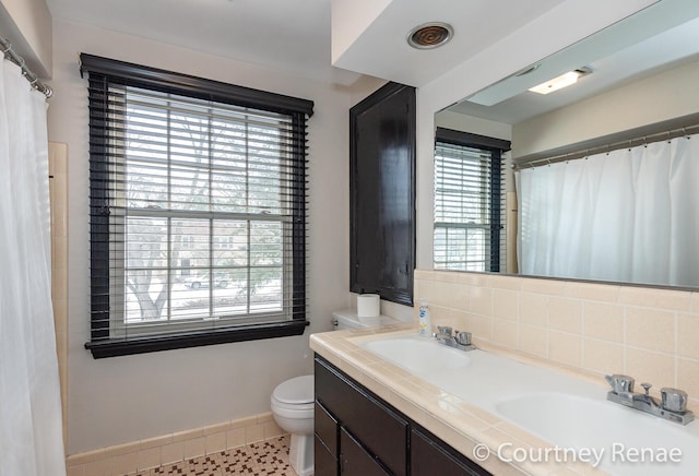 bathroom with tasteful backsplash, a healthy amount of sunlight, toilet, and vanity