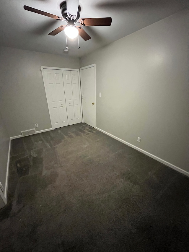 unfurnished bedroom with dark carpet, ceiling fan, and a closet