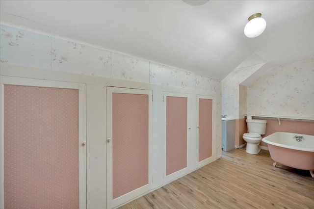 bathroom featuring hardwood / wood-style flooring, lofted ceiling, a washtub, and toilet