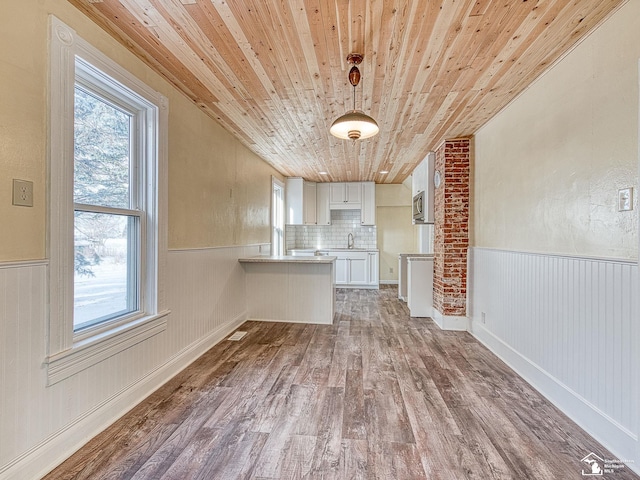 interior space featuring dark hardwood / wood-style floors, stainless steel microwave, white cabinetry, kitchen peninsula, and wooden ceiling