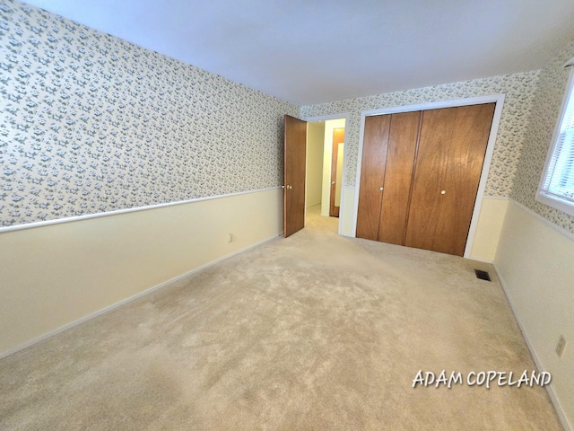 unfurnished bedroom with light carpet and a closet