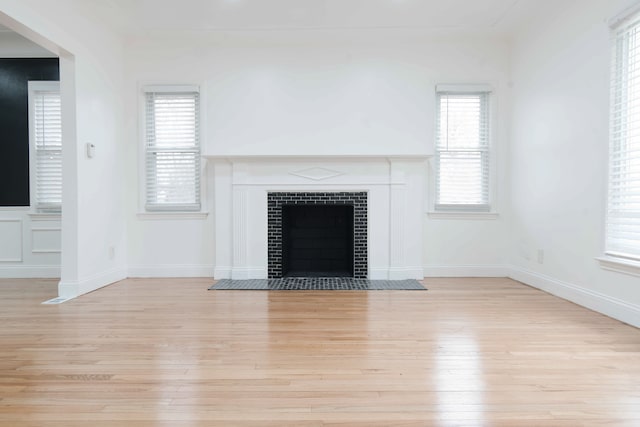 unfurnished living room featuring a tiled fireplace, a wealth of natural light, and light hardwood / wood-style floors