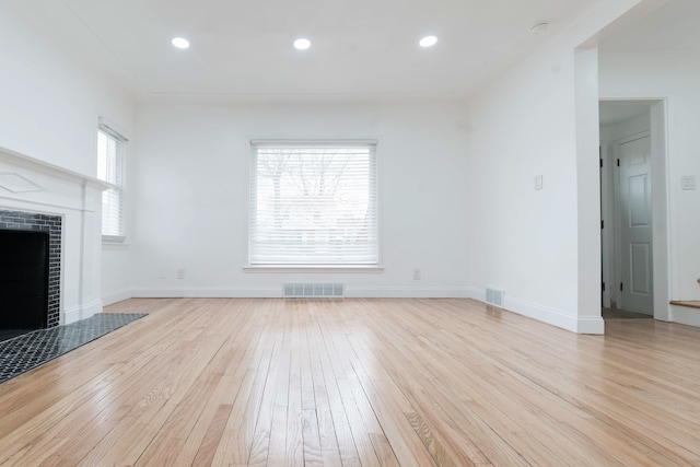 unfurnished living room with a tiled fireplace, a healthy amount of sunlight, and light wood-type flooring