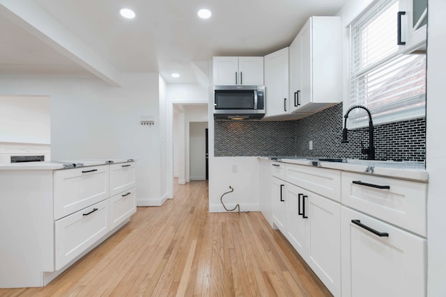 kitchen with sink, white cabinets, decorative backsplash, beam ceiling, and light hardwood / wood-style flooring