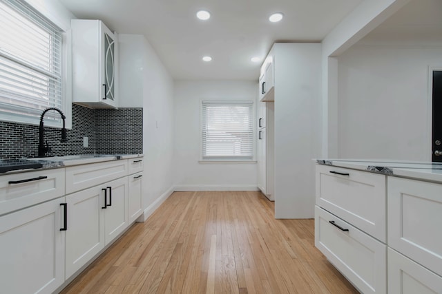 kitchen featuring white cabinetry, sink, backsplash, and light hardwood / wood-style flooring