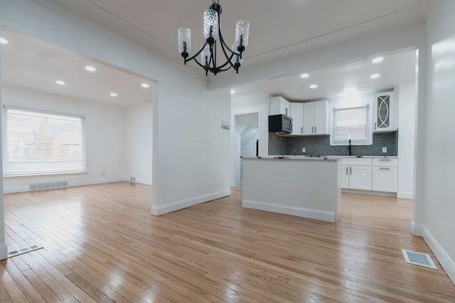 kitchen featuring tasteful backsplash, white cabinets, a chandelier, a center island, and light wood-type flooring