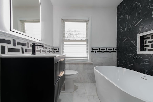 bathroom featuring a washtub, vanity, toilet, and tile walls