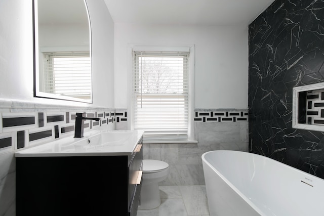 bathroom featuring a washtub, vanity, toilet, and tile walls