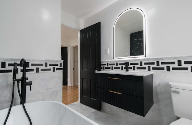 bathroom with vanity, a tub to relax in, tile walls, and toilet