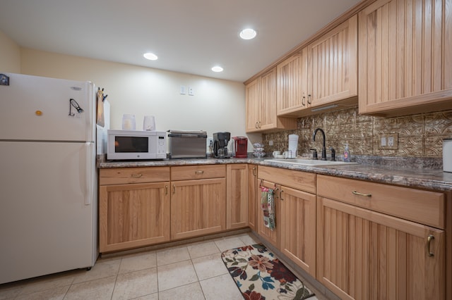 kitchen with sink, white appliances, tasteful backsplash, light tile patterned floors, and dark stone countertops