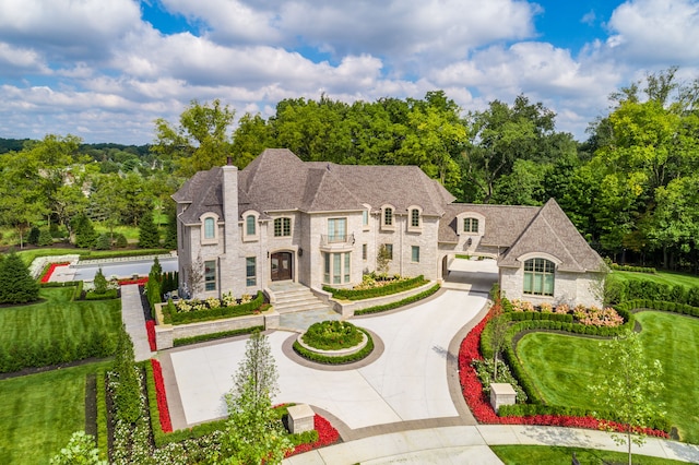 french provincial home featuring stone siding, curved driveway, and a chimney