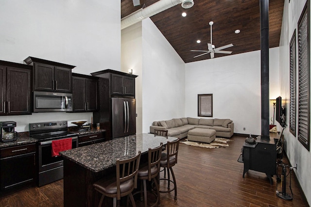 kitchen with dark wood-type flooring, appliances with stainless steel finishes, a center island, a kitchen bar, and dark stone counters