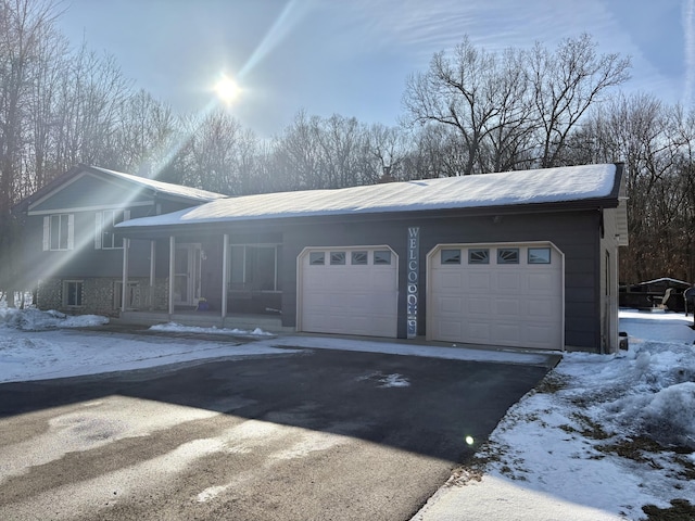 snow covered garage with covered porch and driveway