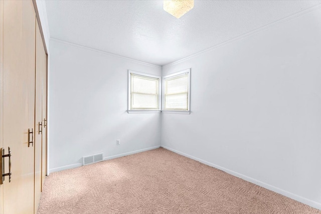 empty room with a textured ceiling, crown molding, and light colored carpet