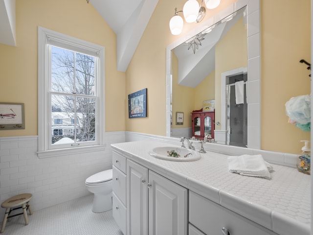 bathroom with tile walls, vanity, vaulted ceiling, tile patterned floors, and toilet