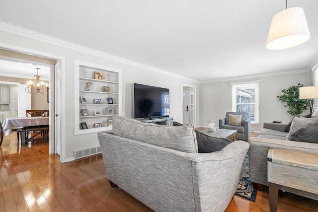 living room featuring built in shelves, ornamental molding, a chandelier, and hardwood / wood-style floors