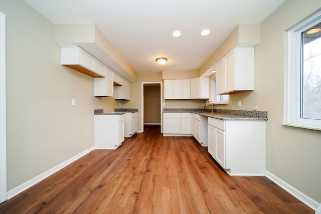 kitchen featuring white cabinetry, dark stone counters, sink, and light hardwood / wood-style flooring