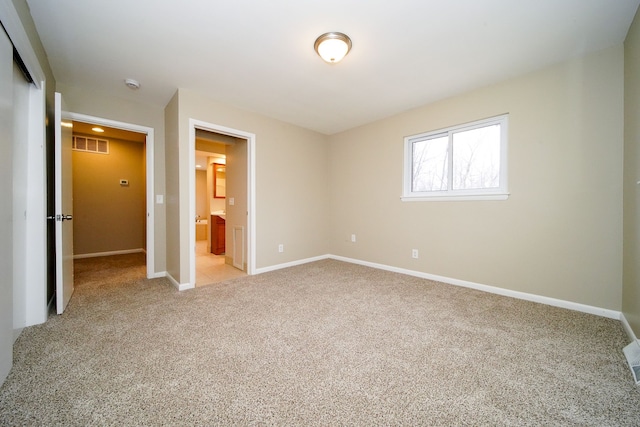 unfurnished bedroom featuring light colored carpet, ensuite bathroom, and a closet