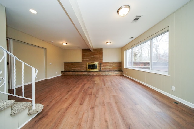 unfurnished living room featuring a fireplace, wood-type flooring, and beam ceiling