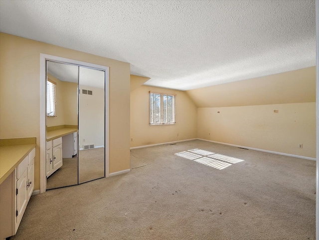 additional living space with light colored carpet, vaulted ceiling, and a textured ceiling