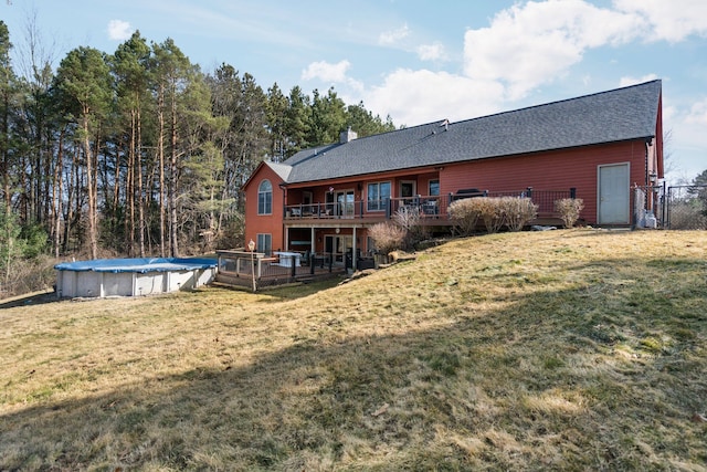 back of property featuring a wooden deck, a lawn, a chimney, and a covered pool