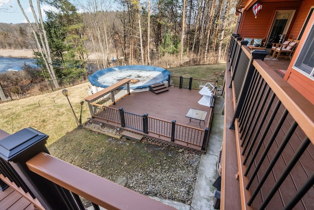 wooden deck featuring a jacuzzi, a view of trees, a yard, and a water view