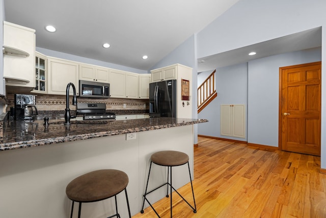 kitchen featuring a peninsula, vaulted ceiling, gas range oven, stainless steel microwave, and black fridge