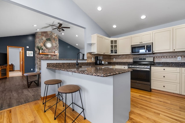 kitchen with a kitchen bar, light wood-type flooring, dark stone countertops, stainless steel appliances, and a sink