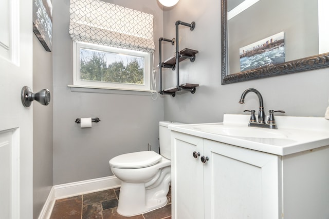 half bathroom with toilet, stone finish flooring, baseboards, and vanity