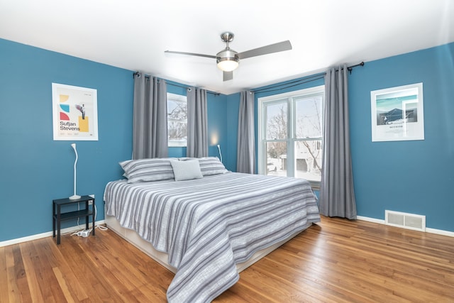 bedroom with a ceiling fan, visible vents, baseboards, and wood finished floors