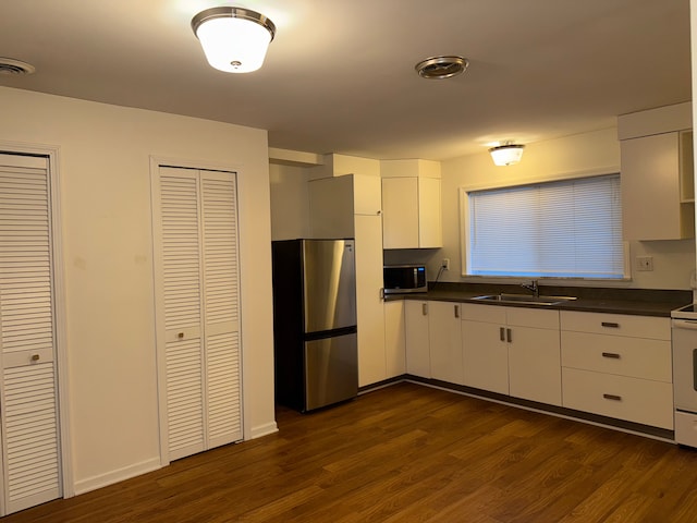 kitchen with stainless steel appliances, dark countertops, dark wood-type flooring, and a sink